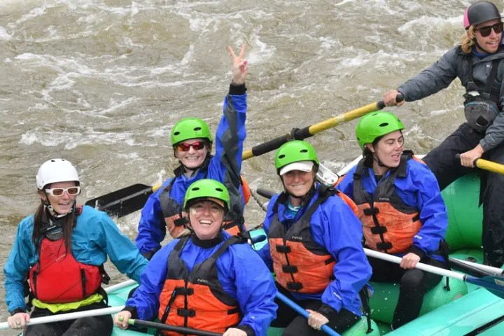 Group whitewater rafting, 5 people with helmets and a guide steering.