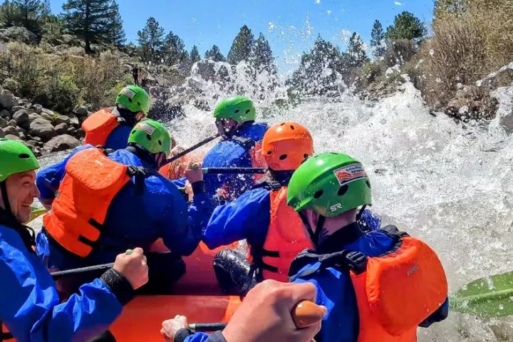 Group rafting on a river, wearing helmets and life jackets surrounded by splashing water.