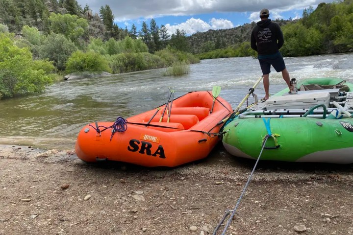 Two rafts on a riverbank; person stands nearby under cloudy sky.