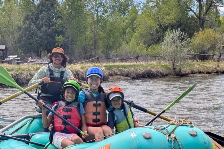 Four people rafting on a river with greenery in the background.