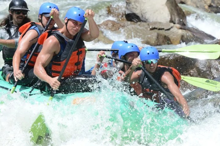 Group of people white-water rafting with helmets and life vests.