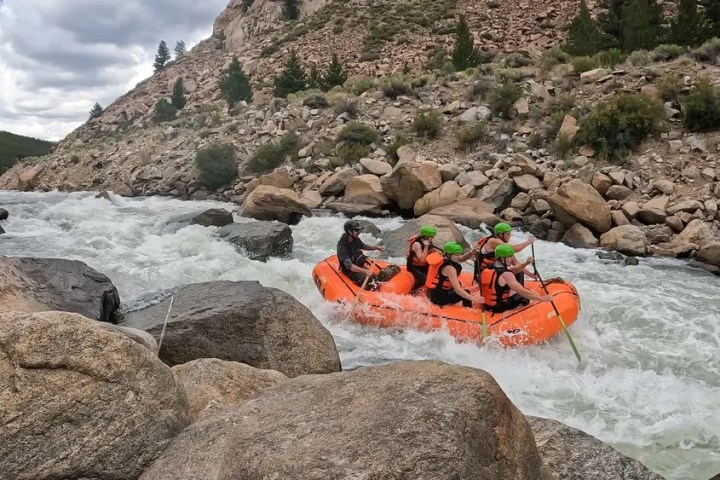 Group of people rafting on a river surrounded by rocks and trees.