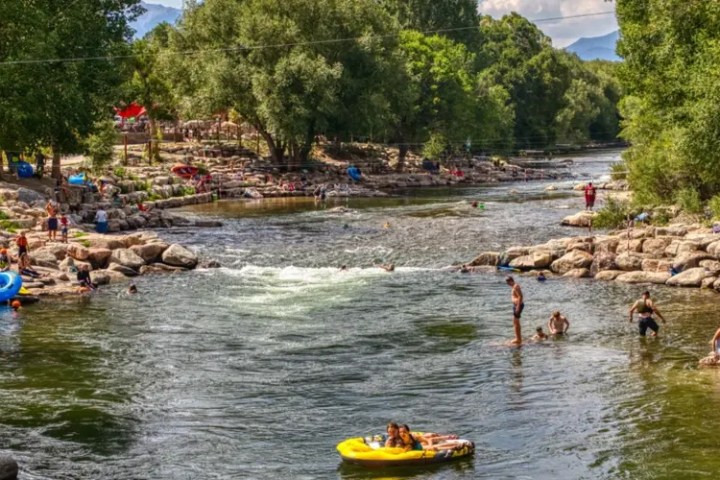 People swimming and tubing in a river surrounded by rocks and trees on a sunny day.