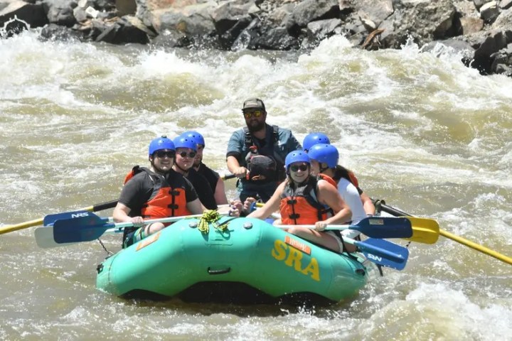 Group of people white-water rafting down a rocky river in an inflatable raft.