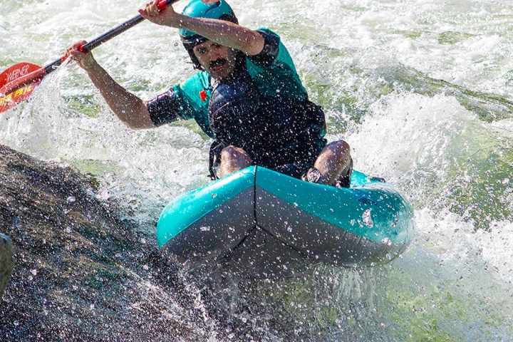 Person kayaking through rough water near a rock formation.