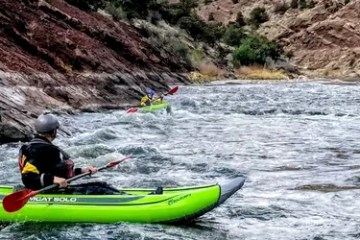 Two people kayaking on a rocky river with rapids.